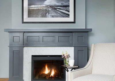 gray wall and fireplace with a white chair of Moonlight residence designed by Elizabeth Robb Interiors